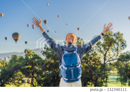 Male tourist standing with colorful hot air balloons floating in the sky behind him, enjoying adventure and sightseeing over Mexico. Travel, tourism, and exploration concept Male tourist standing with colorful hot air balloons floating in the sky behind him, enjoying adventure and sightseeing over Mexico. Travel, tourism, and exploration concept 132390111
