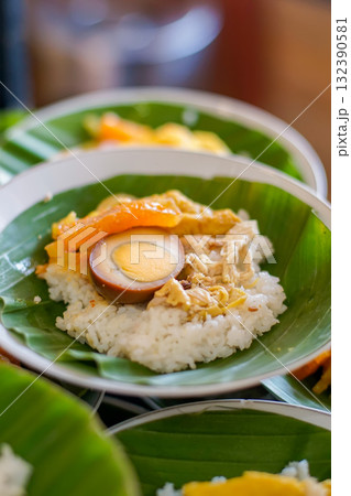 Authentic Indonesian food, Nasi Liwet or Nasi Ayam, white rice served with shredded chicken, marinated egg, and vegetables on banana leaf. Perfect for culinary, cultural, and travel concepts. 132390581