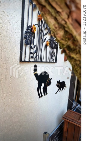 Zelenogradsk, Russia.Two decorative black cat silhouettes with gold collars fixed on a textured white wall, partially framed by a tree. 132391070
