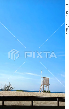 A tall, simple wooden lifeguard tower stands on the sandy beach against the deep blue sea. 132391191