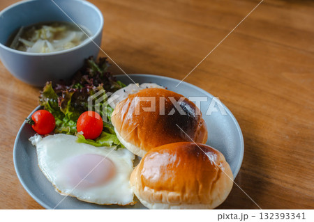 ロールパンと目玉焼き、サラダとスープを添えた洋風の朝食 132393341