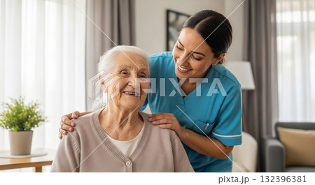 A cheerful female caregiver providing emotional support to a happy elderly woman at home. 132396381