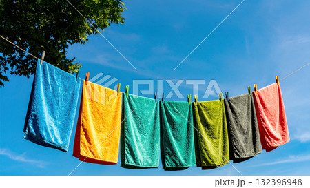 青空の下に干されたカラフルな洗濯物のタオルが、やわらかな風に揺れて陽光と緑が調和 132396948
