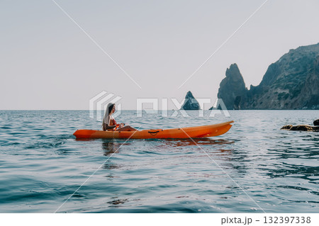 Kayaking Woman Sea Coast - A woman kayaks in the sea with a mountain range in the background. Kayaking Woman Sea Coast - A woman kayaks in the sea with a mountain range in the background. 132397338