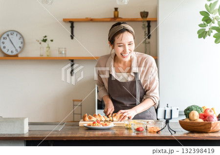 スマホでテレビ電話しながらキッチンで料理をする若いアジア人女性 スマホでテレビ電話しながらキッチンで料理をする若いアジア人女性 132398419