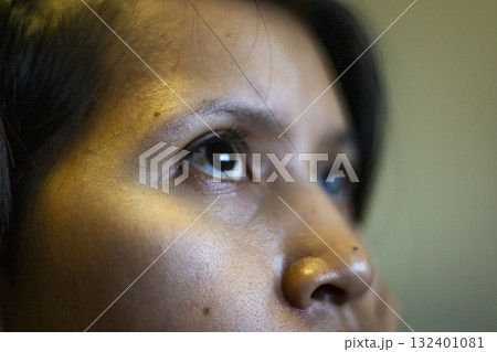 Southeast Asian Woman Gazing At Screen Close Up, A Southeast Asian woman stares intently at a screen, her eyes reflecting soft light, perfect for a focused photo or a digital lifestyle showcase. 132401081