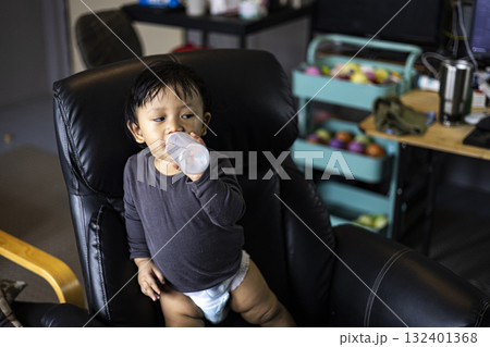 Toddler Drinking Milk Bottle On Office Chair, playful home office moment perfect for parenting ads, family lifestyle campaigns, and baby product promotions. Toddler Drinking Milk Bottle On Office Chair, playful home office moment perfect for parenting ads, family lifestyle campaigns, and baby product promotions. 132401368