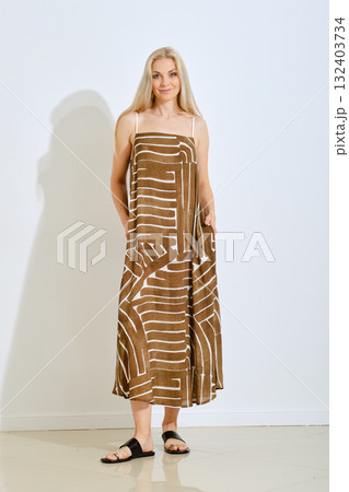 Model showcases a stylish brown dress with white pattern in a modern studio setting 132403734