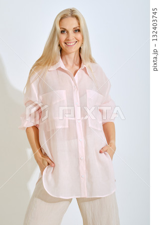 Model poses in light pink oversized shirt and beige pants in bright studio setting Model poses in light pink oversized shirt and beige pants in bright studio setting 132403745
