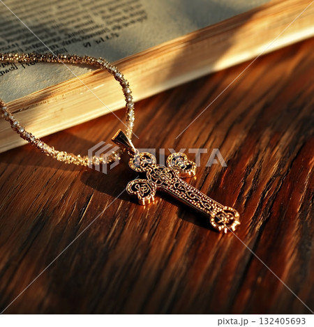 Gold cross necklace is on a wooden table next to a book Gold cross necklace is on a wooden table next to a book 132405693