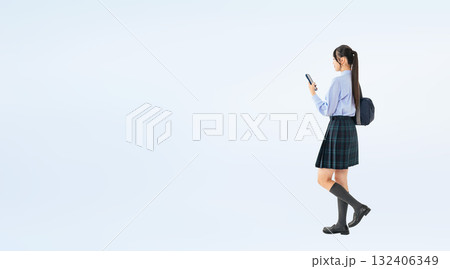 スマホを見ながら歩く制服の女子学生の全身写真 132406349