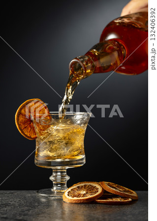 Rum or whiskey is poured from a bottle into a glass with ice. Rum or whiskey is poured from a bottle into a glass with ice. 132406392