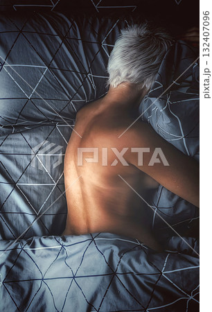 Top-Down View of a Person with Platinum Blonde Hair Lying Asleep on Geometric Patterned Bedding. 132407096