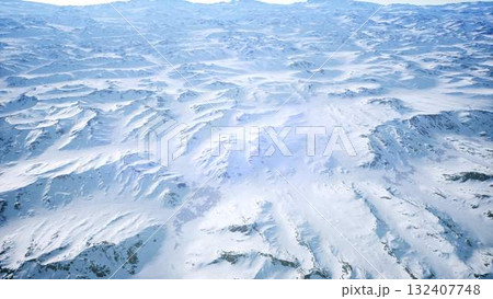 Amidst the vast expanse of snow, majestic mountain peaks rise under a clear sky. The quiet beauty of winter creates a tranquil, breathtaking scene that invites exploration and adventure. 132407748