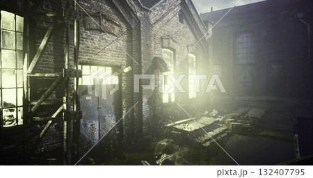 An old factory structure is enveloped in dim light, with broken windows revealing a haunting atmosphere. Overgrown plants and debris surround the entrance, showcasing years of neglect. 132407795