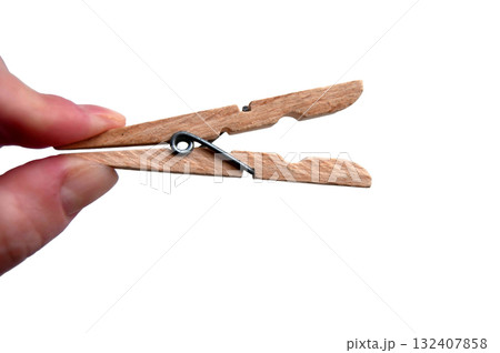 A wooden clothespin in hand isolated. An open clothes peg held in fingers. A wooden clothespin in hand isolated. An open clothes peg held in fingers. 132407858