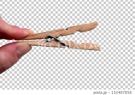 A wooden clothespin in hand isolated. An open clothes peg held in fingers. A wooden clothespin in hand isolated. An open clothes peg held in fingers. 132407858