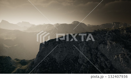 Rugged mountain peaks stretch across the horizon, bathed in a gentle glow as morning light spills over the landscape. Soft shadows emphasize the contours, creating a tranquil and mystical setting. 132407936