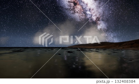 Under a canopy of stars, the tranquil sea reflects the wonders of the galaxy. Waves softly lap against the shore as the Milky Way illuminates the night sky, creating a breathtaking view. 132408384