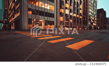 As dusk settles over the city, vibrant lights reflect on wet pavement. The crosswalk stands empty, framed by modern buildings showcasing a blend of glass and steel in the urban landscape. 132408475