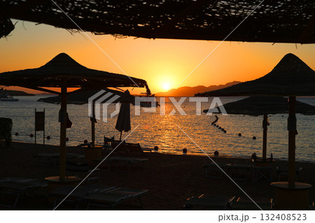 Sunrise over the sea against the backdrop of thatched umbrellas on the beach 132408523