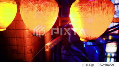 Illuminated yellow lanterns hang against a colorful backdrop filled with lights and shadows, creating a warm atmosphere in a bustling urban nightlife setting. 132408591
