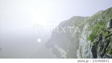 Majestic cliffs rise above a tranquil sea, illuminated by the soft glow of the early morning sun. A peaceful beach lies below, surrounded by lush greenery and rocky formations. 132408631