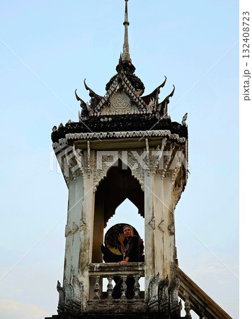 Blonde tourist standing in a beautiful, ornate, weathered Buddhist temple bell tower against a bright blue sky. Blonde tourist standing in a beautiful, ornate, weathered Buddhist temple bell tower against a bright blue sky. 132408723