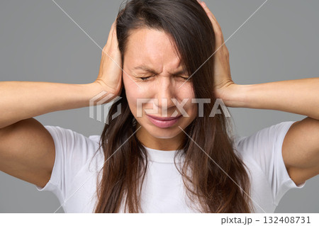 Close-up of woman covering ears tightly with eyes closed in reaction to loud 132408731