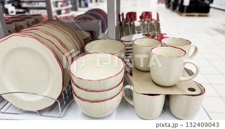 Ceramic dishes with red trim displayed in a store setting, featuring cups, bowls, and plates Ceramic dishes with red trim displayed in a store setting, featuring cups, bowls, and plates 132409043
