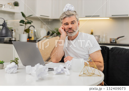 Middle-aged man writes ideas at table using laptop fights creative block tired unmotivated at home Middle-aged man writes ideas at table using laptop fights creative block tired unmotivated at home 132409073