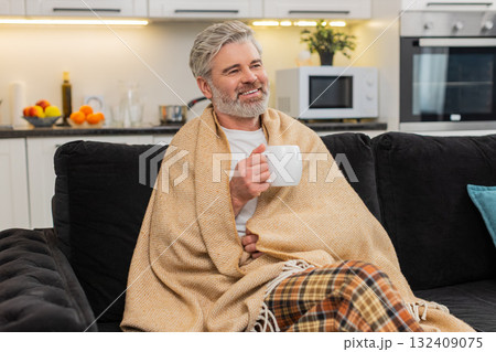 Middle-aged mature man takes small sip of herbal tea warms hands cozy mood autumn style calm rest 132409075