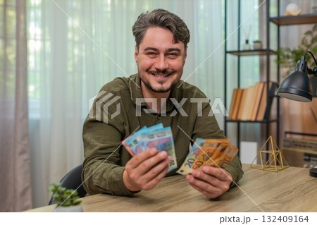Middle-aged man counts cash smiling showing big financial success euro bills wealth at table desk Middle-aged man counts cash smiling showing big financial success euro bills wealth at table desk 132409164