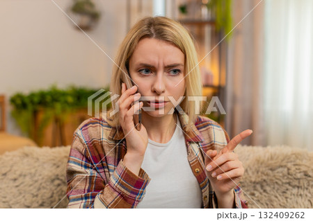 Woman rejecting call on smartphone at home, showing hand gesture to say no with irritated expression Woman rejecting call on smartphone at home, showing hand gesture to say no with irritated expression 132409262