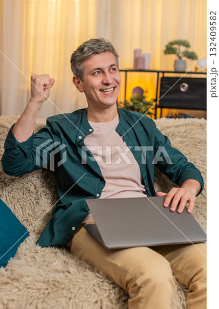 Young man closes laptop with smile and shows victory gesture after finishing productive online work Young man closes laptop with smile and shows victory gesture after finishing productive online work 132409582
