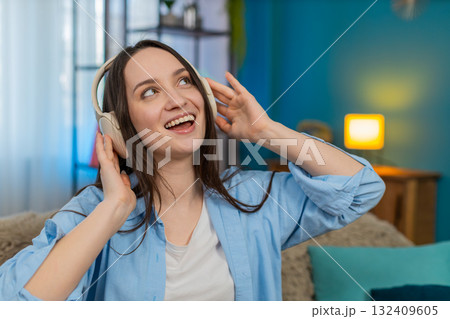 Young woman wearing wireless headphones on sofa dancing smiling happily enjoying favorite song 132409605