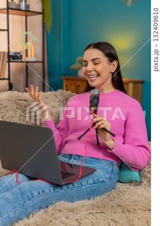 Young woman sitting on sofa recording podcast speaking seriously into microphone with focused look Young woman sitting on sofa recording podcast speaking seriously into microphone with focused look 132409610