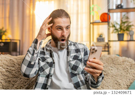 Young man typing fast at home, smartphone deal hunt, excitement, sudden wow, big online find 132409671
