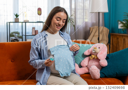 Pregnant woman looking at baby cloth and pacifier, preparing pregnancy, expecting baby, childbirth 132409698