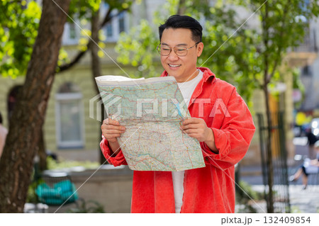 Asian man tourist exploring city street sightseeing holding paper map check direction searching way 132409854