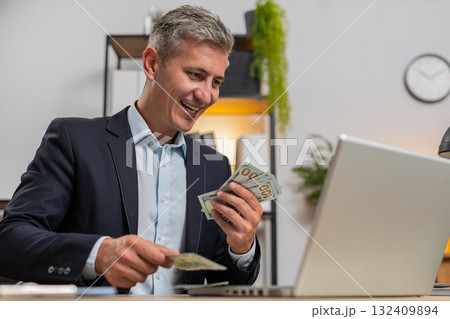 Caucasian young businessman in suit working on laptop PC counting money cash at home office desk 132409894