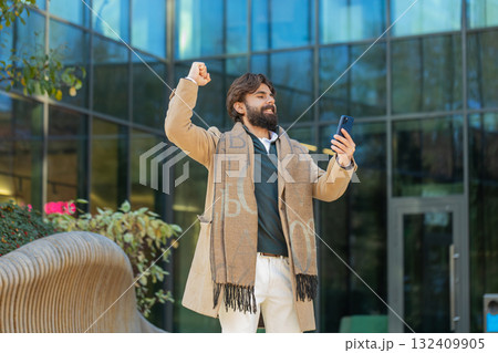 Happy Indian man using smartphone celebrating victory win good message news on downtown city street Happy Indian man using smartphone celebrating victory win good message news on downtown city street 132409905