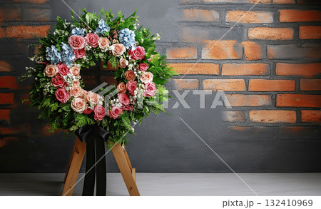 Funeral wreath of flowers with black ribbon on wooden stand against grey background, space for text 132410969