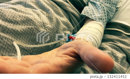 A patient hand with an intravenous catheter in a hospital bed, symbolizing healthcare, treatment, illness, and recovery A patient hand with an intravenous catheter in a hospital bed, symbolizing healthcare, treatment, illness, and recovery 132411452