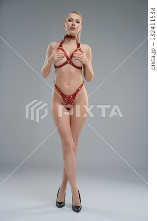 Woman poses confidently in leather belts in a studio setting with dramatic lighting Woman poses confidently in leather belts in a studio setting with dramatic lighting 132411538