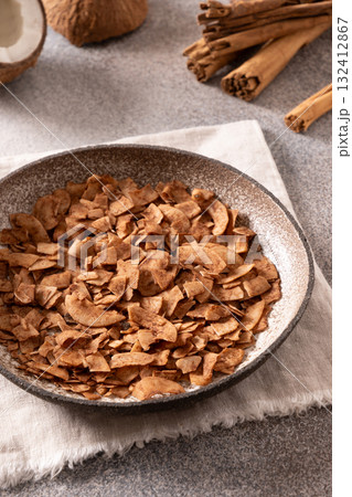 Coconut chips with cinnamon in glass jar on gray background. Healthy sugar free dessert. Vertical format. Sri lankan local snack. Coconut chips with cinnamon in glass jar on gray background. Healthy sugar free dessert. Vertical format. Sri lankan local snack. 132412867