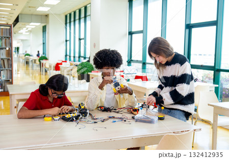 High view of multiracial teen boy and girls enjoy and fun with assemble the robot as their home work in public library. 132412935
