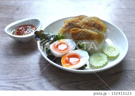 deep fried slice gourami fish topping plain rice with soft boiled egg and fresh vegetable on plate dipping spicy sweet fish sauce  132413123