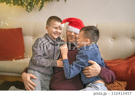 Boys hug their father in a New Year's red hat. The family is having fun on Christmas Eve. 132413457