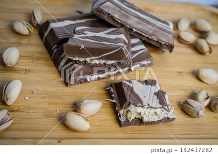 Medium shot of broken chocolate pieces with whole pistachios scattered around. Perfect for food photography, desserts, confectionery, healthy snacks, and gourmet concepts. Medium shot of broken chocolate pieces with whole pistachios scattered around. Perfect for food photography, desserts, confectionery, healthy snacks, and gourmet concepts. 132417282